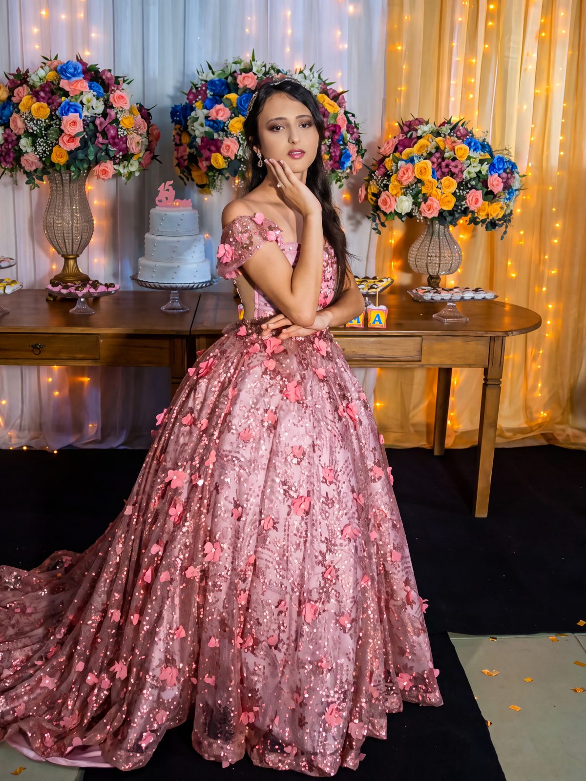 Debutante ao lado da mesa do bolo, entre arranjos de flores